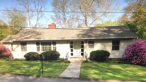A single-story house with a front porch, a brick chimney, and a driveway leading to the entrance.