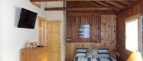 A wooden cabin bedroom with a bed, dresser, and television.