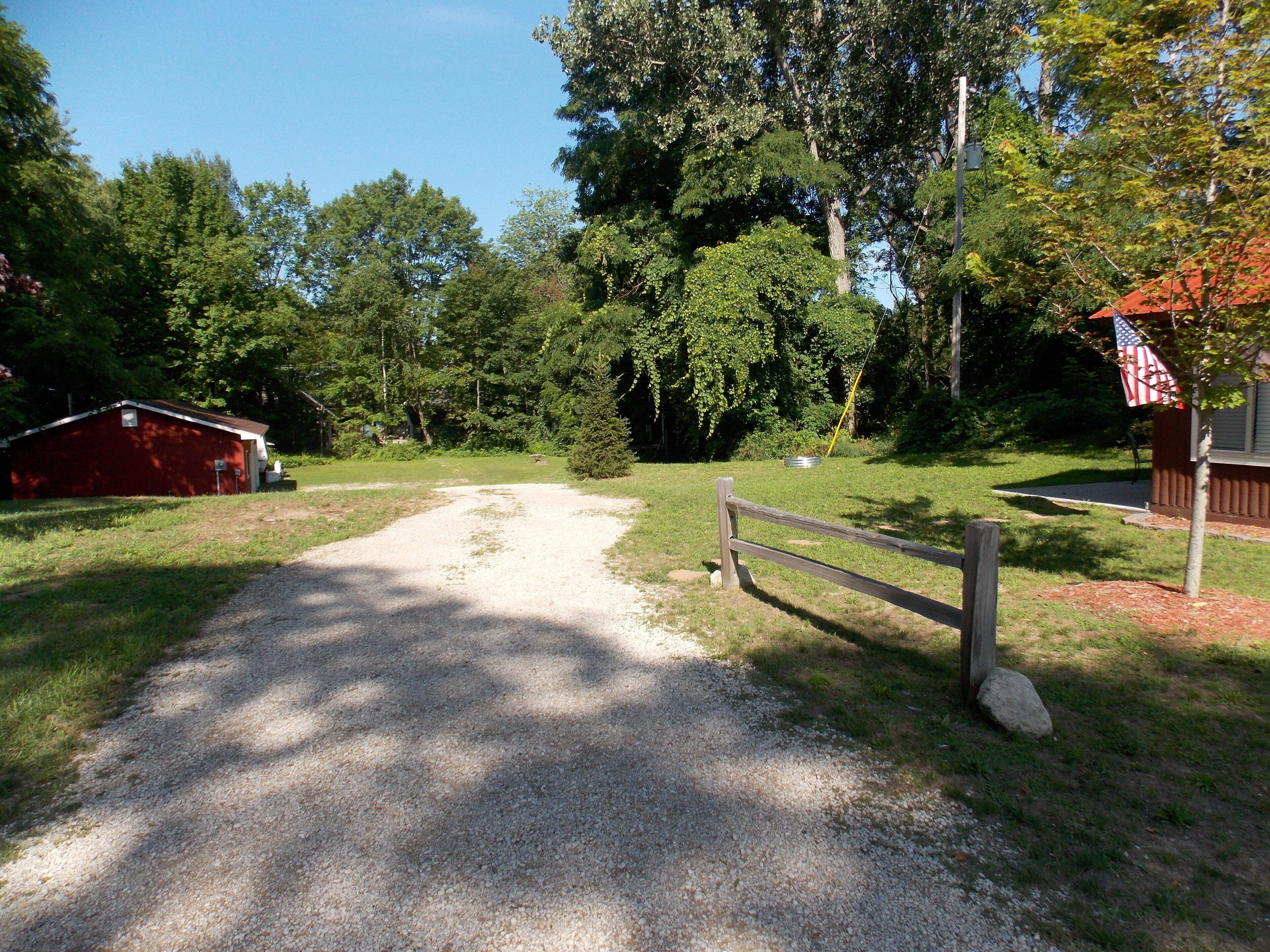 A gravel path leading to a red barn and a wooden fence.
