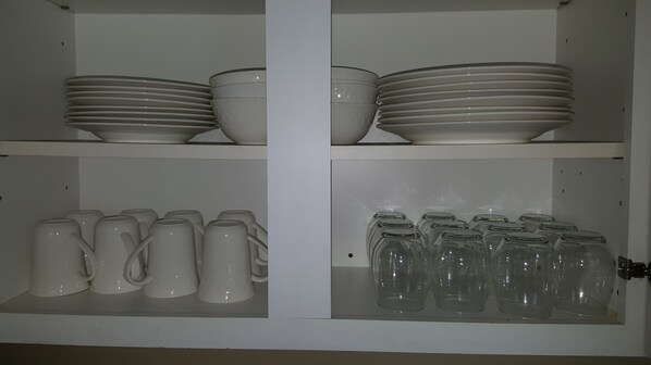 A cabinet with shelves containing white plates, bowls, mugs, and glasses.