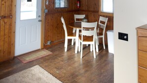 L’intérieur d’un chalet en bois, avec une table à manger, des chaises, un ventilateur de plafond, une porte blanche et une fenêtre.
