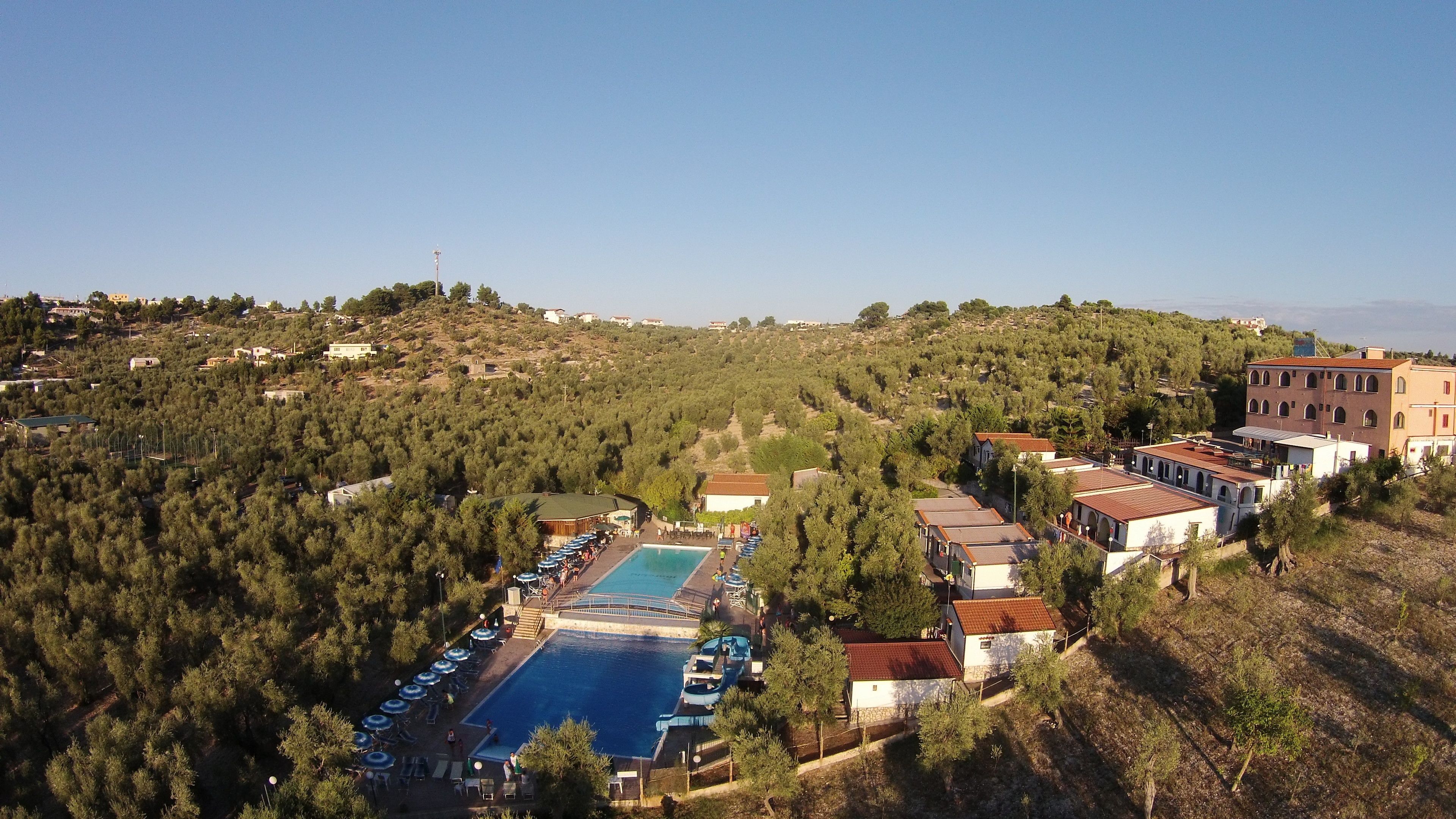 Vista aérea de un complejo turístico con piscina, varias edificaciones y un paisaje montañoso.
