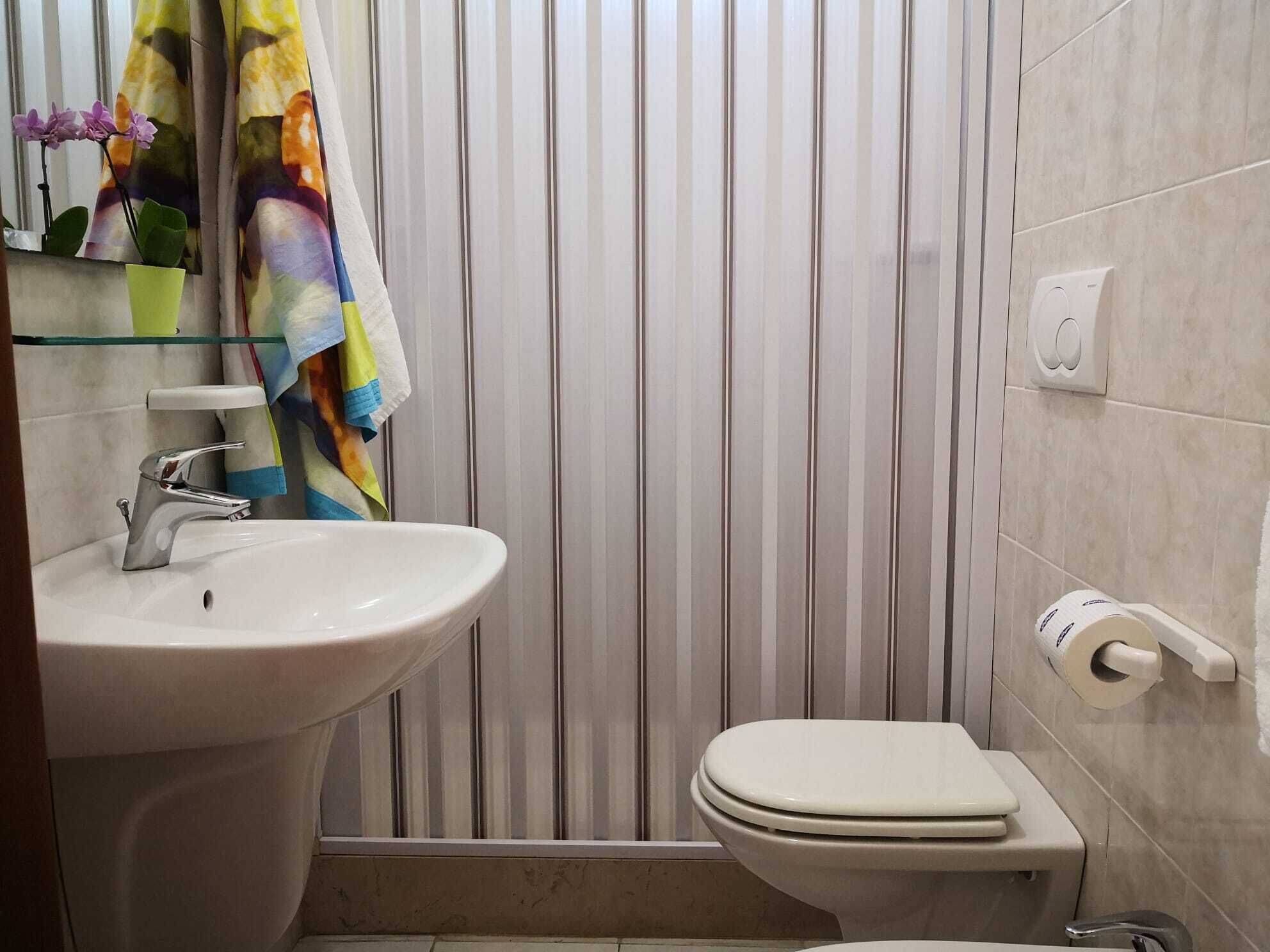 Kylpyhuone, jossa on valkoinen pesuallas, wc ja raidallinen seinä.