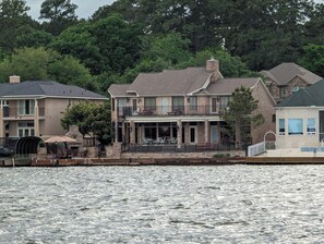 A waterfront property with a large house featuring a balcony, a covered patio, and a view of the water.