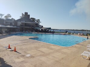 A swimming pool with lounge chairs and umbrellas, a building with a stone facade, and a view of the water.
