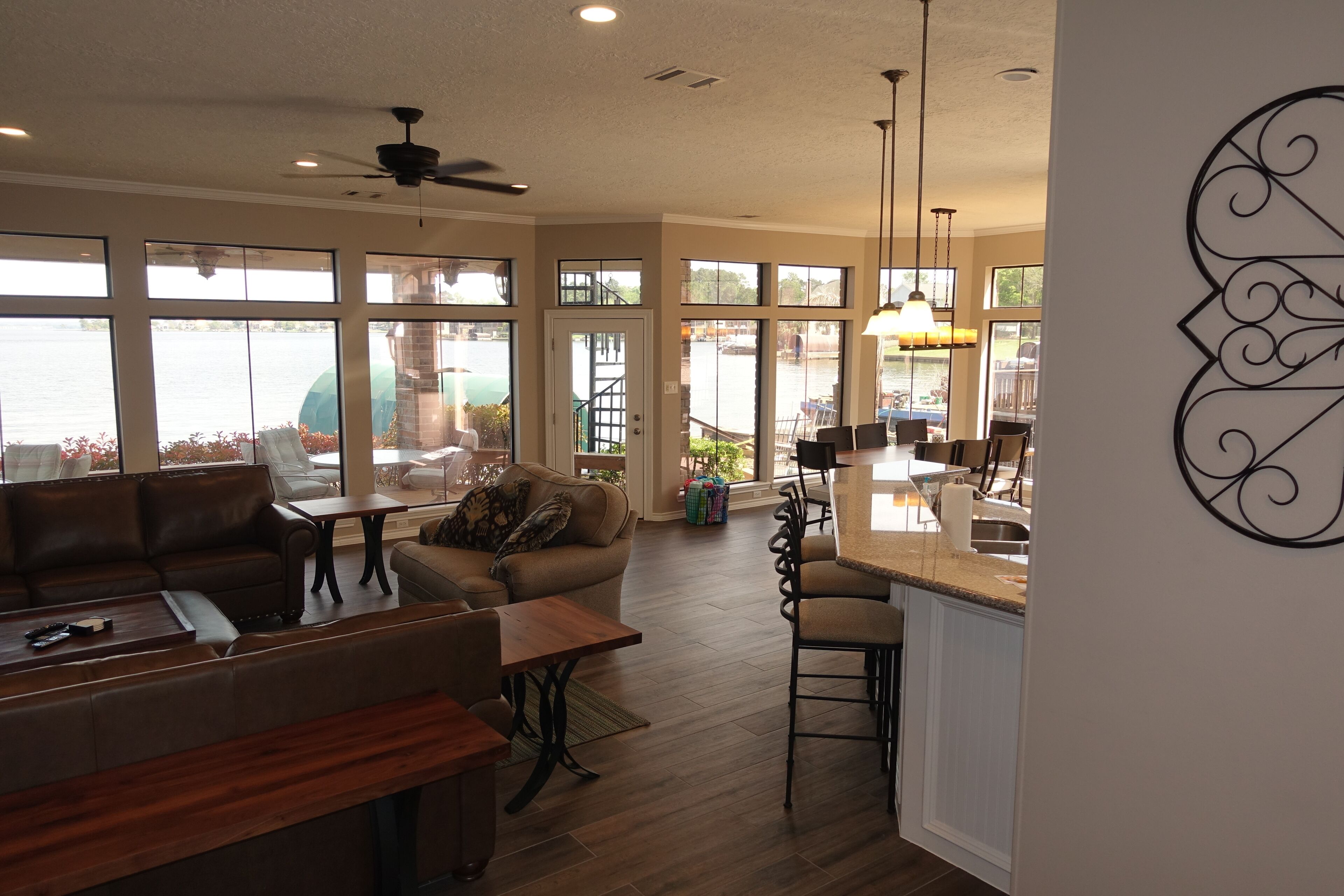 A spacious living area with a large window overlooking a body of water, a ceiling fan, and a kitchen area with a bar stool.