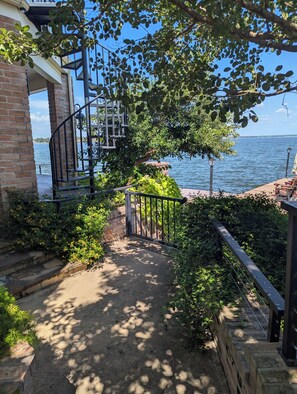 A pathway leading to a waterfront property with a brick wall, a metal gate, and a view of the sea.