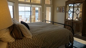 Un dormitorio con cama, un ventanal grande, vista al agua y un armario de madera.