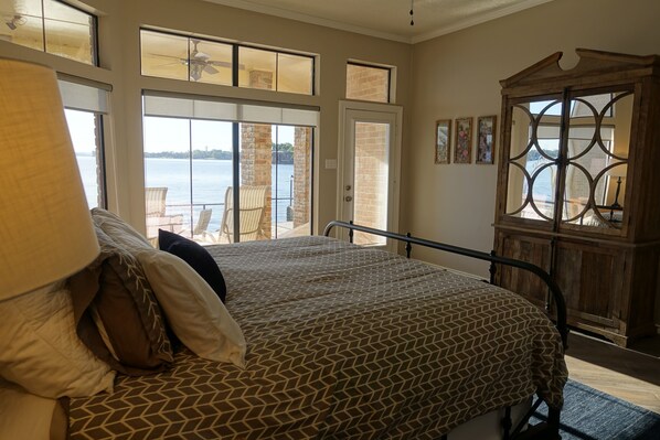 A bedroom with a bed, a large window, a view of the water, and a wooden cabinet.