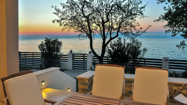 A terrace with two white cushioned chairs and a wooden table, overlooking a sunset over the sea. - Balconies on the sea - the garden apartment (Thassos)