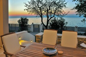 A terrace with two white cushioned chairs and a wooden table, overlooking a sunset over the sea. - Balconies on the sea - the garden apartment (Thassos)