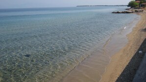 A beach with clear shallow waters, a sandy shore, and a distant shoreline with buildings. - Balconies on the sea - the garden apartment (Thassos)
