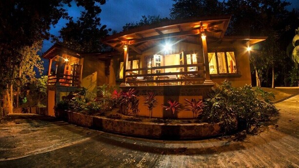 A two-story wooden house with a balcony, surrounded by a landscaped garden with various plants. - Quinta Teca with two pools near Playa Hermosa beach (Playa Hermosa)