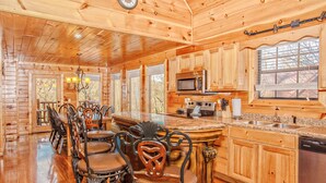 A wooden cabin interior with a kitchen, dining area, and bar seating. - 💦Skinny Dippin🌲Private Indoor Pool, Hot Tub, Theater & Game Room (Sevierville)