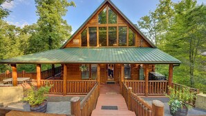 A log cabin with a green metal roof, wooden deck, and a wooden staircase leading to the entrance. - 💦Skinny Dippin🌲Private Indoor Pool, Hot Tub, Theater & Game Room (Sevierville)