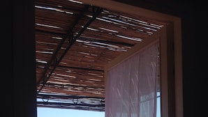 A balcony with a view of the sea, a wooden ceiling, and a metal railing.