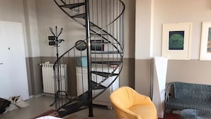 A living room with a spiral staircase, a yellow armchair, a wicker chair, and a radiator.