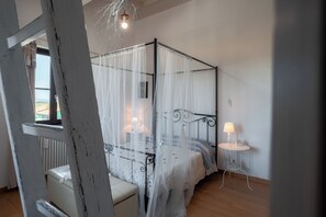 Ein Bett mit Baldachin, ein Nachttisch mit Lampe und Blick ins Freie durch ein Fenster.