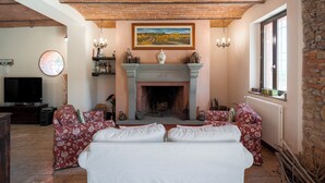 A living room with a fireplace, two sofas, a television, and a stone wall. - Farmhouse with swimming pool 2 km away from the sea (Piombino (LI))