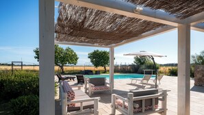 Eine Terrasse im Freien mit Pool, Holzmöbeln und einem Reetdach.