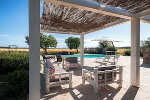 Eine Terrasse im Freien mit Pool, Holzmöbeln und einem Reetdach.