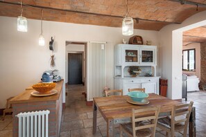 Una cocina rústica con una mesa de madera, lámparas colgantes y un armario blanco.