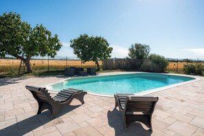 Una piscina con sillones de descanso, una terraza de madera y vistas al campo.