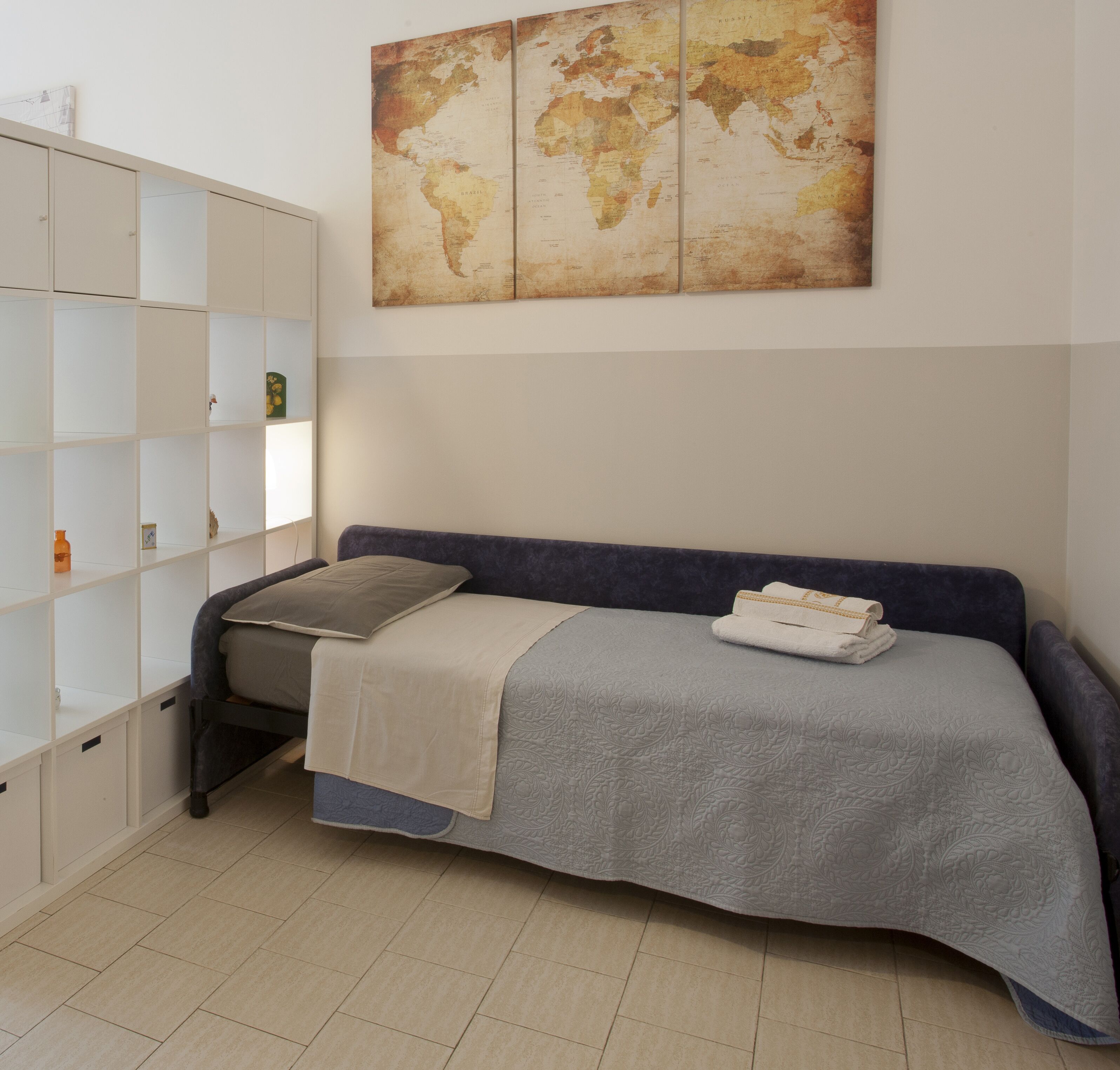 Une chambre bien rangée, avec un lit, une armoire et une carte du monde accrochée au mur.