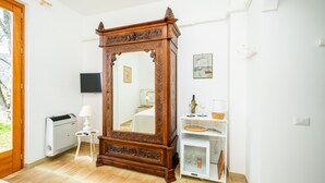 Ein Zimmer mit einem großen hölzernen Spiegel, einem weißen, an der Wand befestigten Fernseher, einem kleinen Tisch mit Lampe und einem weißen Schrank mit Regalen.