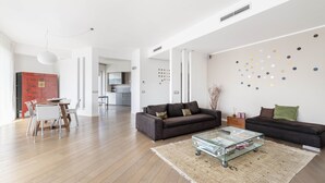 Una sala de estar amplia con piso de madera, dos sofás, una mesa de centro y un comedor con mesa y sillas.