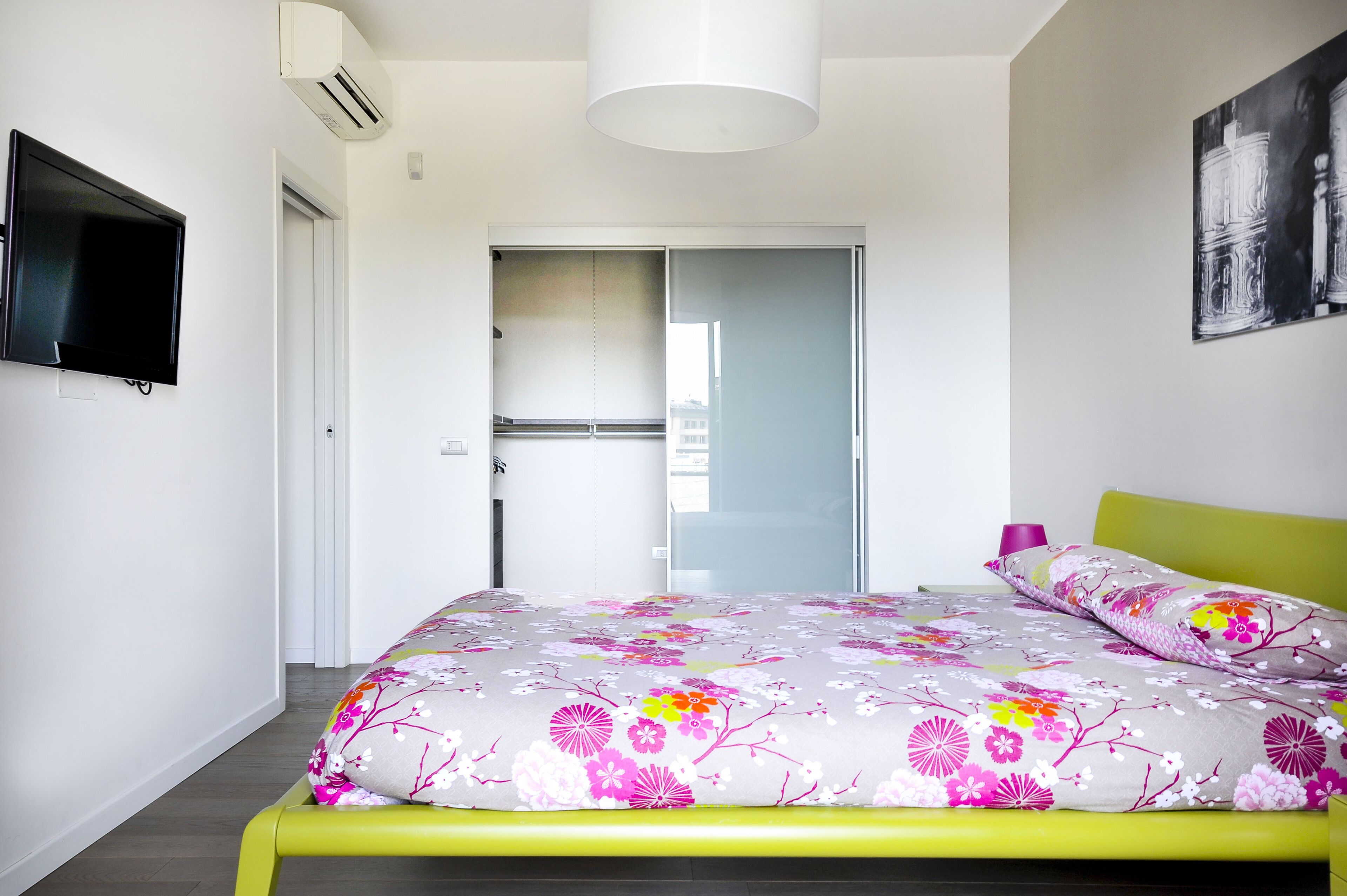 Een slaapkamer met een bed, een televisie, een deur en een raam.