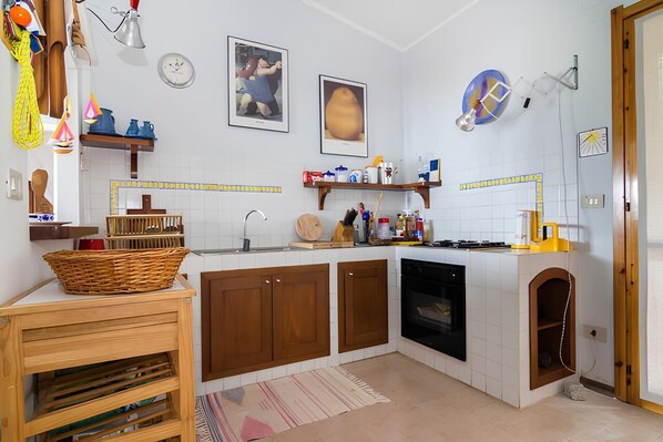 A compact kitchen with wooden cabinets, a stove, and a dishwasher. There are various kitchen items on the counter and shelves.