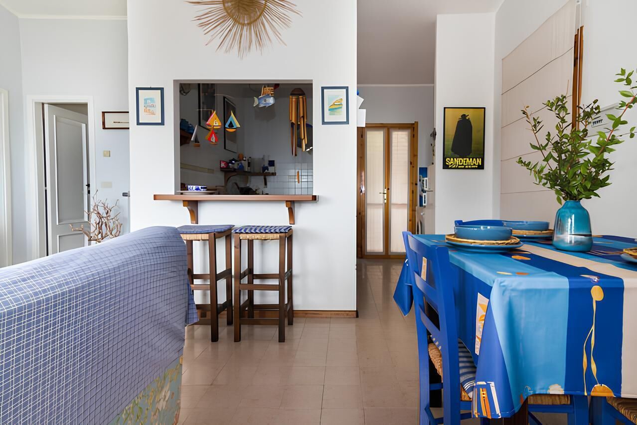A dining area with a table set for two, a bar area with stools, and a kitchen visible in the background.