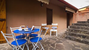 A patio with a round table and blue chairs, a wooden door, and a stone staircase. - Casa Relax between sea and sky (Bosa)