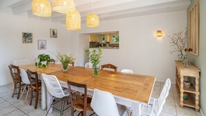 Comedor con mesa de madera, sillas blancas y lámparas de mimbre colgantes.