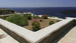 A rooftop garden with plants and flowers, a stone wall, and a view of the sea.