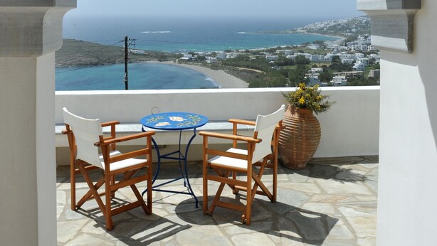 A stone archway leading to a balcony with a table and chairs, overlooking a coastal view.