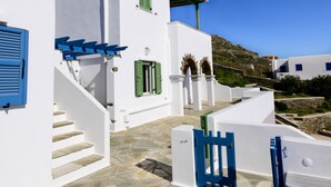 A white building with green shutters and a blue door, a stone staircase, and a clear blue sky.
