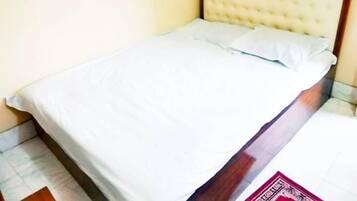 Een bed met houten frame en een gestoffeerd hoofdeinde, witte beddengoed en een betegelde vloer.
