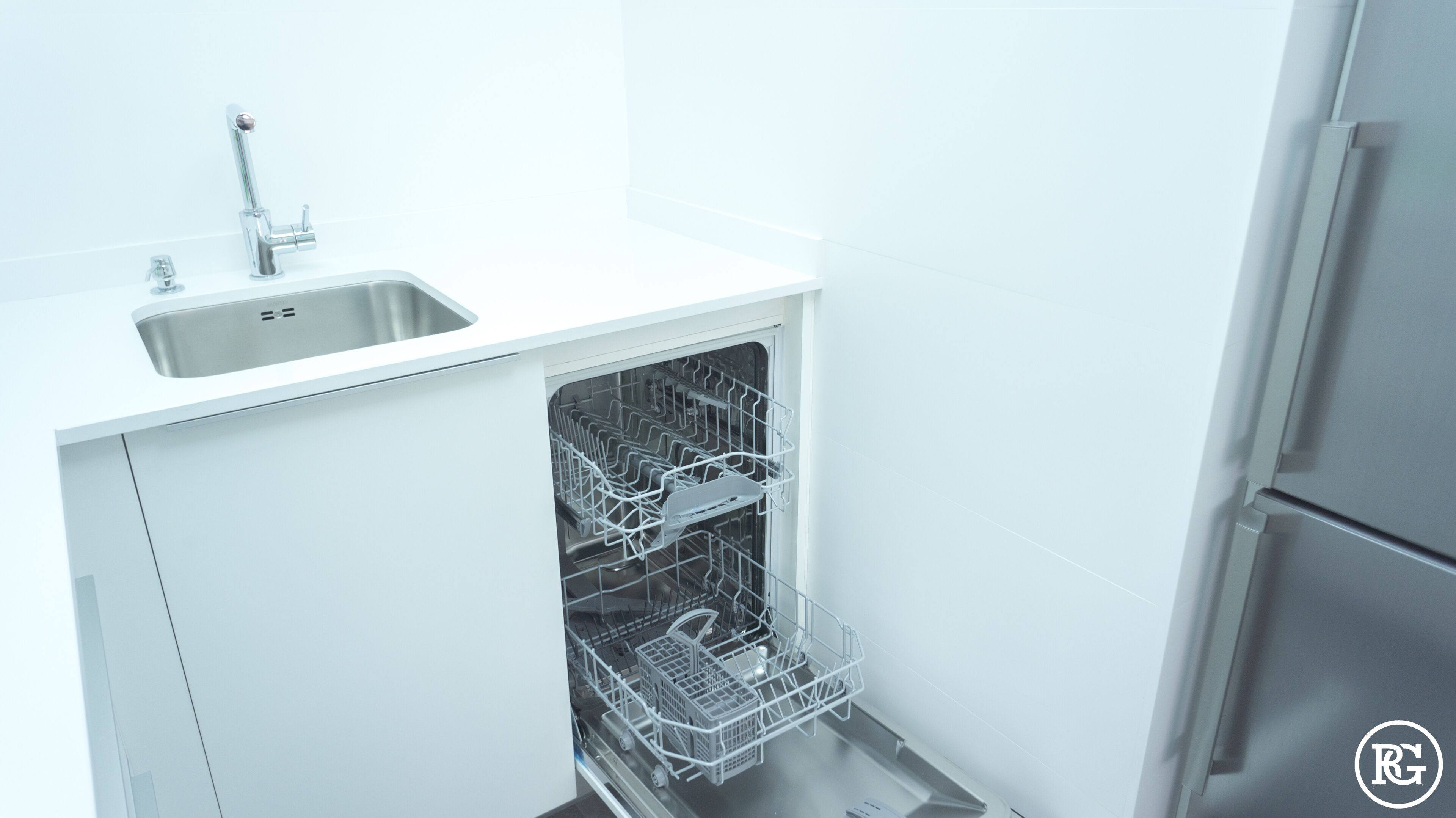 A compact kitchen with a built-in dishwasher, a stainless steel sink, and a refrigerator.