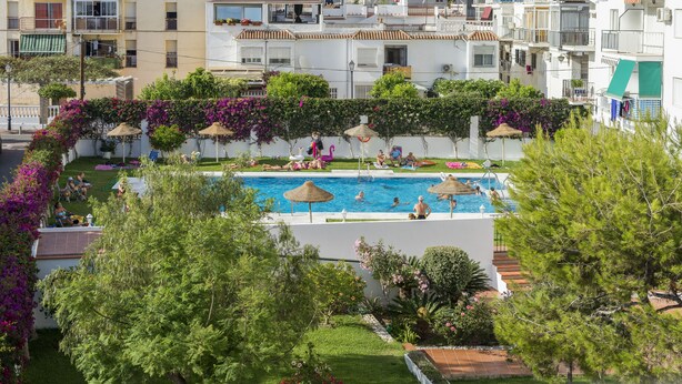 A swimming pool surrounded by lush greenery and white buildings with balconies. - 2 Bed Apartment with communal pool (Nerja)