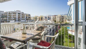 A balcony with a table set for two, overlooking a residential area with multiple buildings and a clear sky. - 2 Bed Apartment with communal pool (Nerja)
