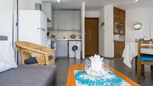 A compact living space with a sofa, dining table, wicker chair, kitchenette, washing machine, and wooden cabinets. - 2 Bed Apartment with communal pool (Nerja)