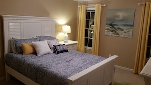 Uma cama bem arrumada com roupa de cama estampada, uma mesa de cabeceira com abajur e um quadro na parede.