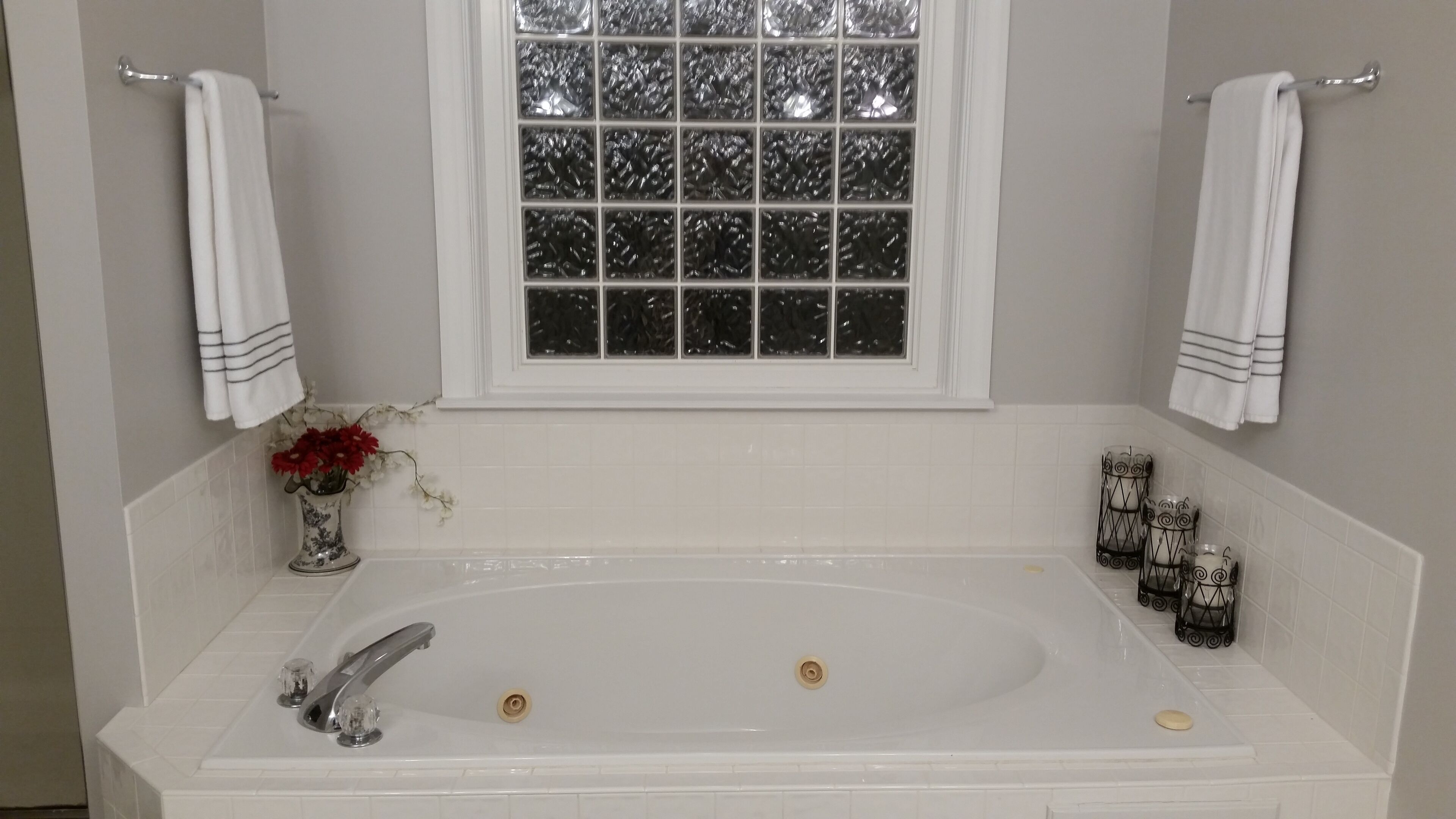 A bathroom with a large bathtub, a window with frosted glass, and two towels hanging on towel bars.