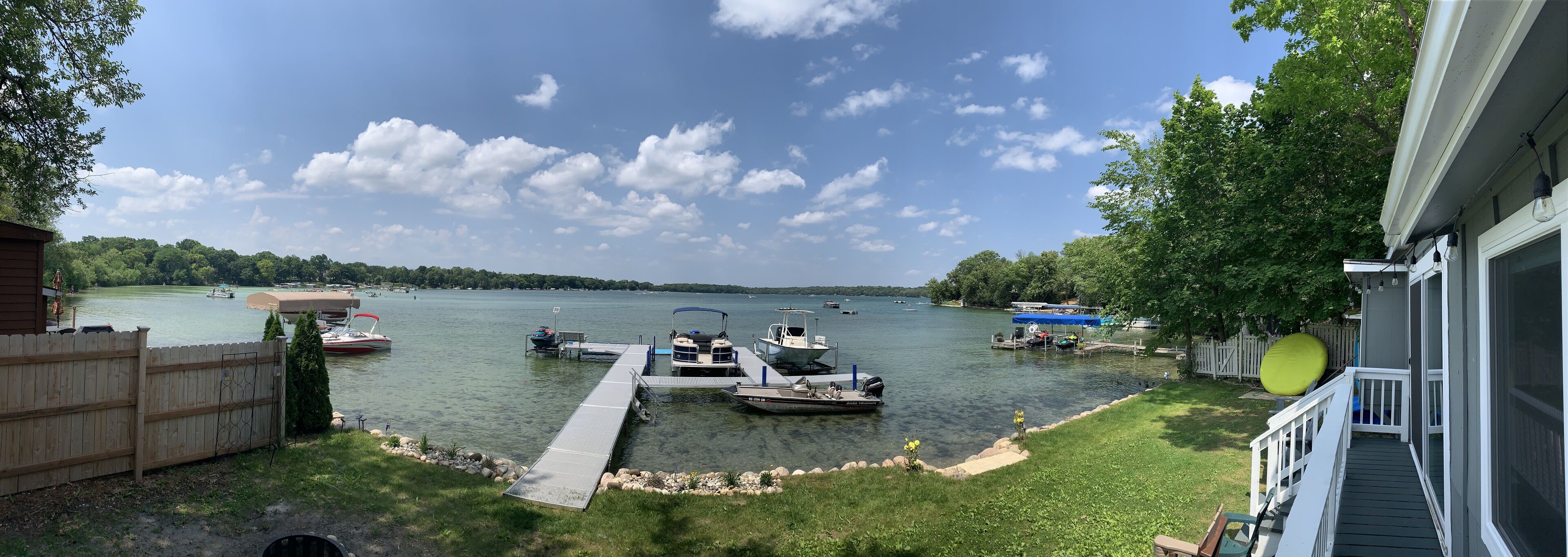 Une jetée au bord du lac avec des bateaux, une terrasse en bois et une maison avec un porche.