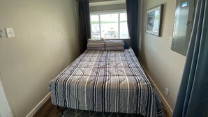 Um quarto com cama, ventilador de teto, janela com cortinas e porta.