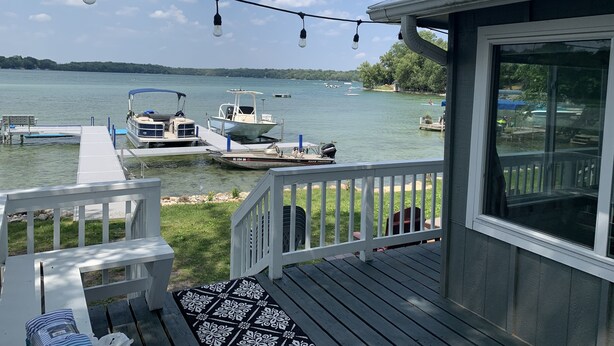 Um terraço com vista para um lago, barcos atracados e uma área coberta com um banco.