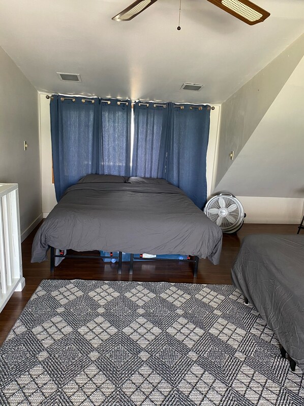 Un dormitorio con cama, ventilador de pie y alfombra estampada.