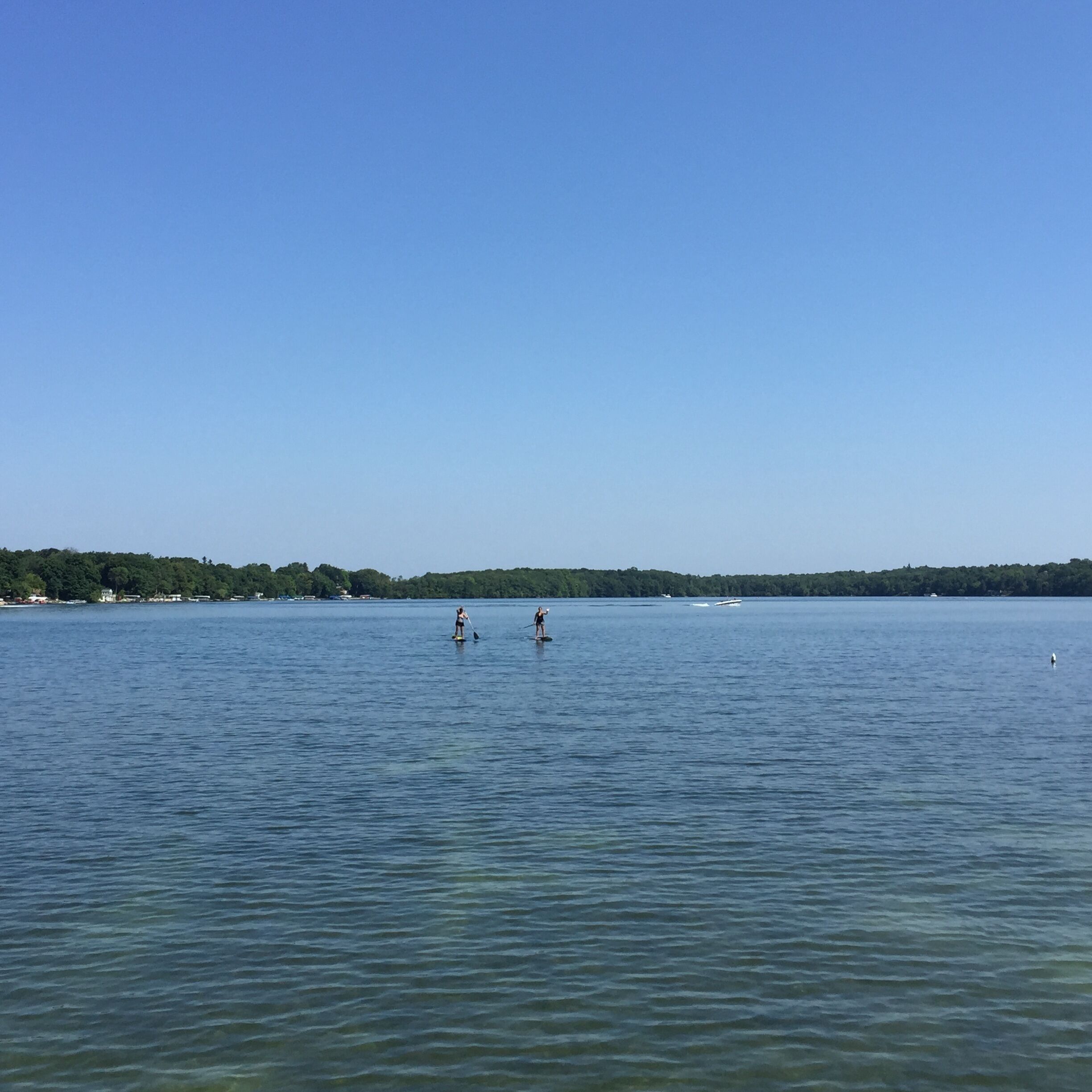 A calm lake with two people paddleboarding.